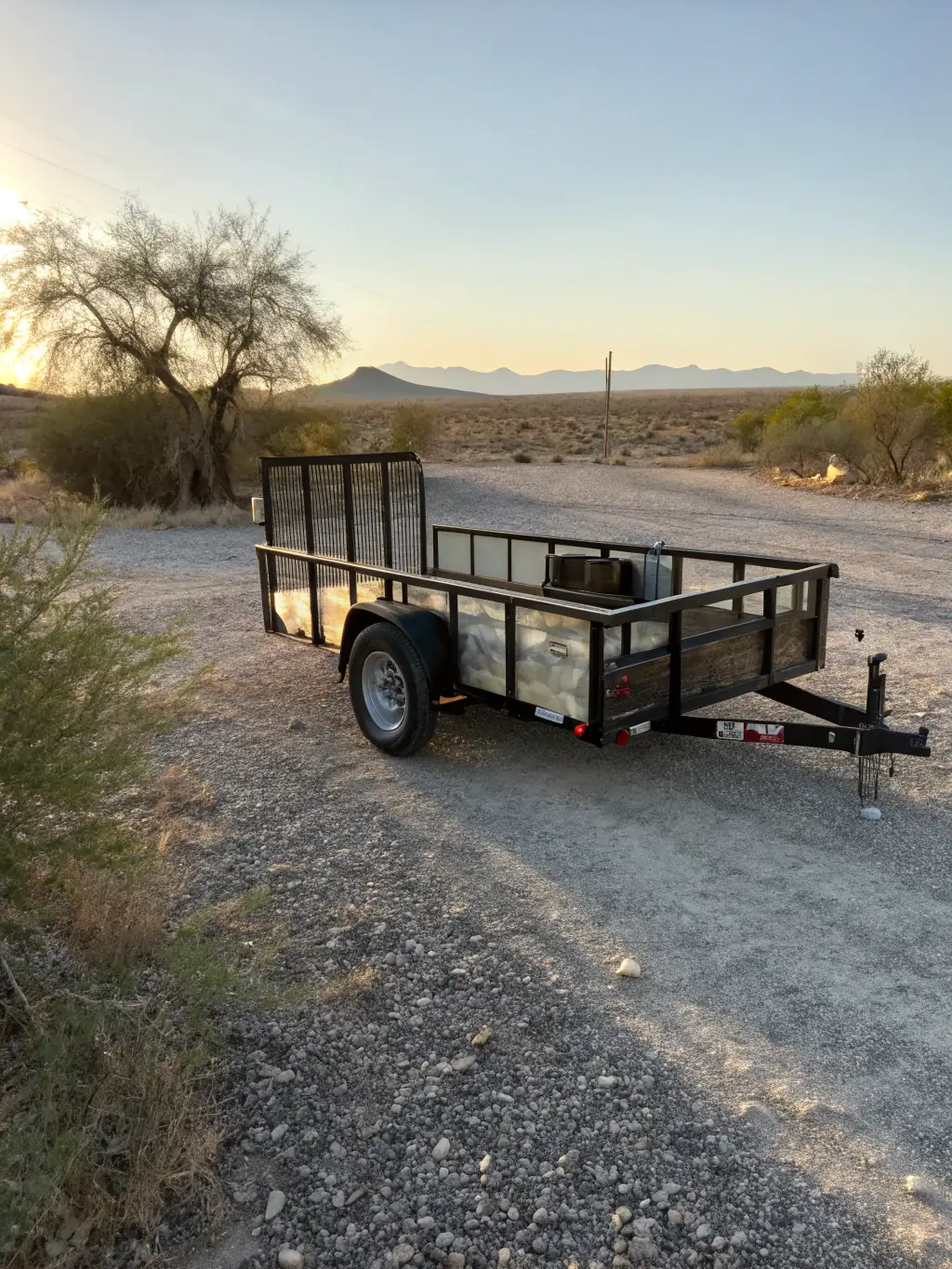 A sturdy utility trailer with a ramp, suitable for hauling landscaping materials or ATVs, shown in a natural outdoor setting.